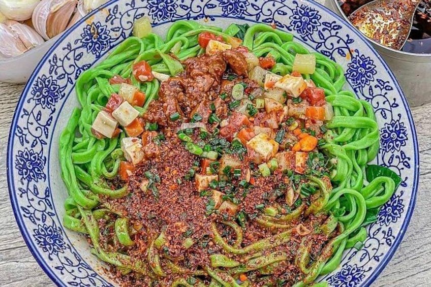 A plate of green pasta with a tomato-based sauce and diced vegetables. 2