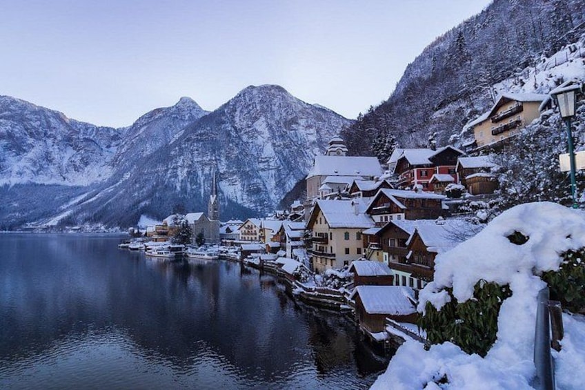A snow-covered lakeside village with traditional houses, a church, and mountains in the background. 5