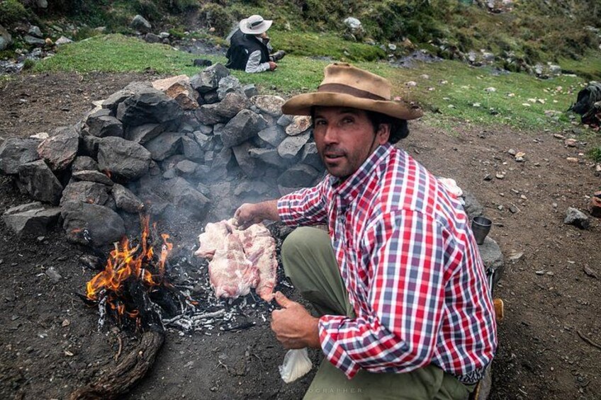 A person cooking meat over an open fire in a natural setting. 2
