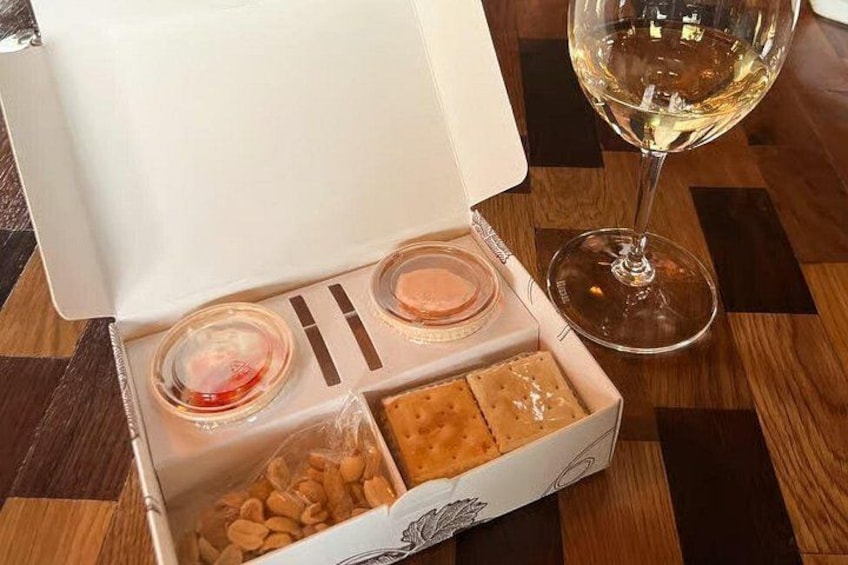 A box with snacks and a glass of white wine on a wooden table. 2