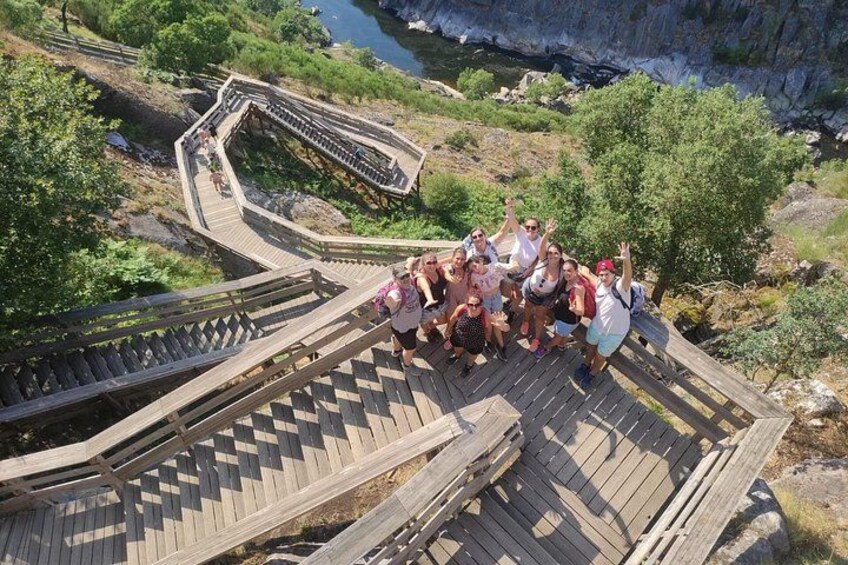 Un groupe de personnes se trouve sur un escalier en bois, avec une rivière et des falaises en arrière-plan. 2