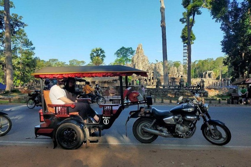 A tuk-tuk on a road with a temple in the background. 2