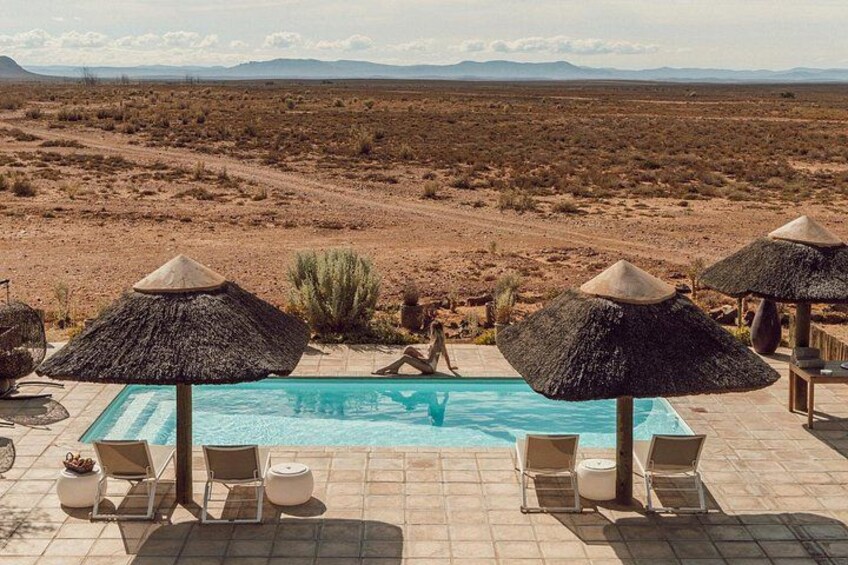 A swimming pool with lounge chairs and thatched umbrellas, set against a desert landscape. 4