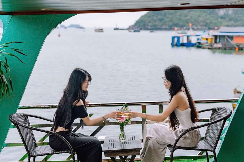 Two women sitting at a table with a view of a body of water and boats in the background. 1