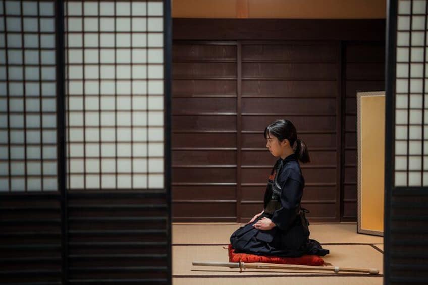Une personne vêtue d’un costume traditionnel est assise sur un tatami dans une pièce dotée de portes coulissantes. 3