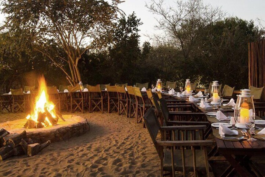 A beachside dining setup with tables, chairs, a fire pit, and lanterns. 3