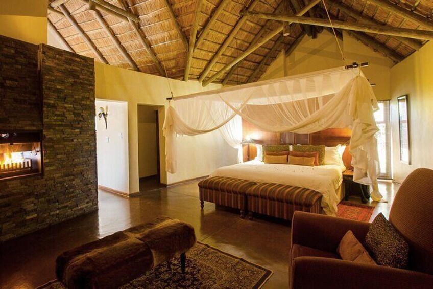 A spacious bedroom with a large bed, a wooden bench, a cushioned chair, a stone fireplace, and a canopy bed. 4