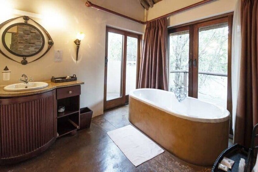 A bathroom with a freestanding bathtub, a vanity with a mirror, and a window with curtains. 5