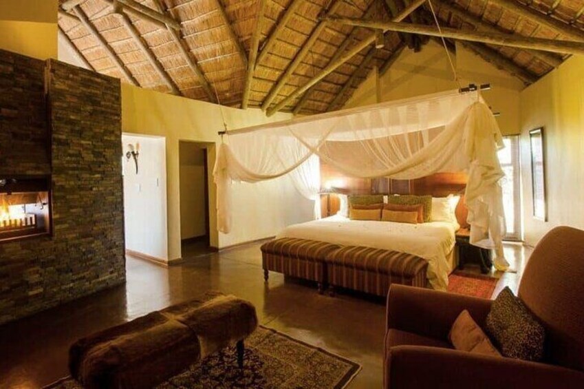 A bedroom with a canopy bed, a stone fireplace, and a rustic ceiling. 2