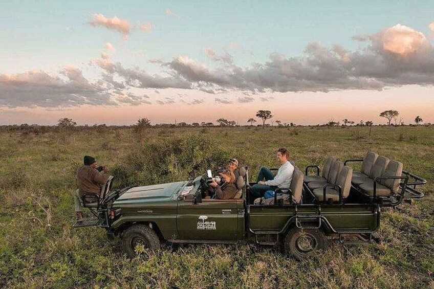 A safari vehicle with passengers, surrounded by a grassy savanna landscape with sparse trees. 2