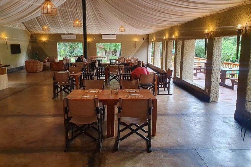 An indoor dining area with tables and chairs, a draped ceiling, and large windows. 3