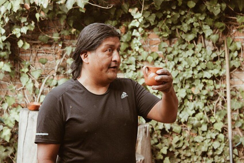 A person holding a cup, standing in front of a wall covered with green ivy. 3