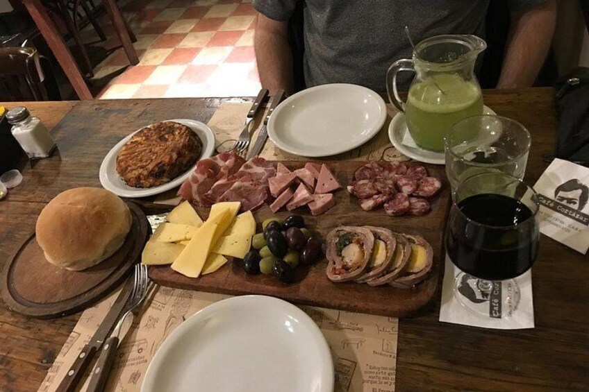 Una comida con diferentes carnes, queso, aceitunas y una bebida sobre una mesa de madera. 5