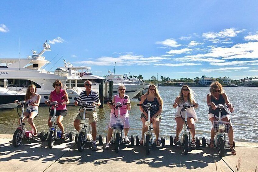 A group of people riding electric scooters on a dock by the water. 4