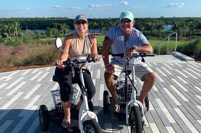 Two people on a dock with a body of water and greenery in the background. 3
