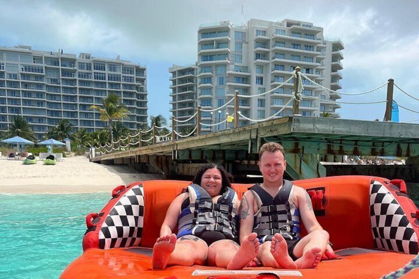 Two people on a boat with a checkered pattern, a beach, and hotel buildings in the background. 1