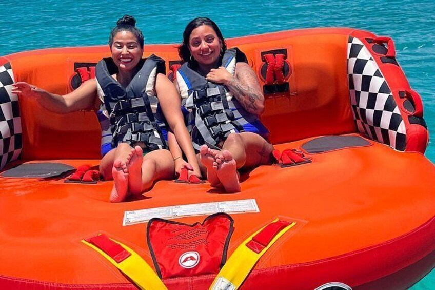 Two people on an inflatable raft with life jackets, a red life vest, and a checkered cushion. 5