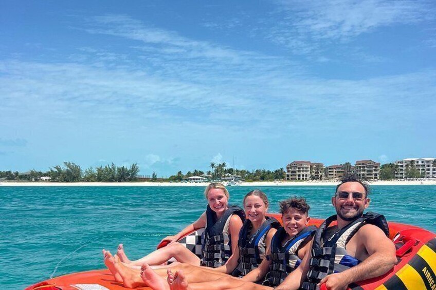 A group of people on a red inflatable raft in turquoise water with a clear sky and buildings in the background. 3