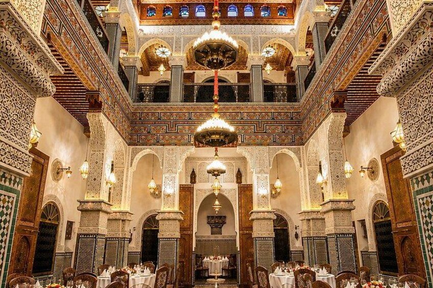 An ornate interior with intricate tile work, arched doorways, and hanging chandeliers. 1