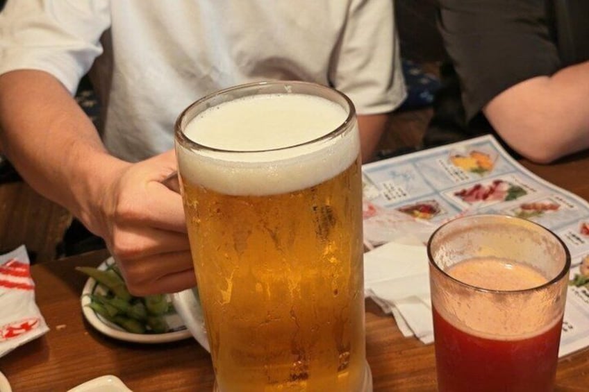 A tall glass of beer with a foamy head, a smaller glass of red drink, and a menu with food illustrations. 5