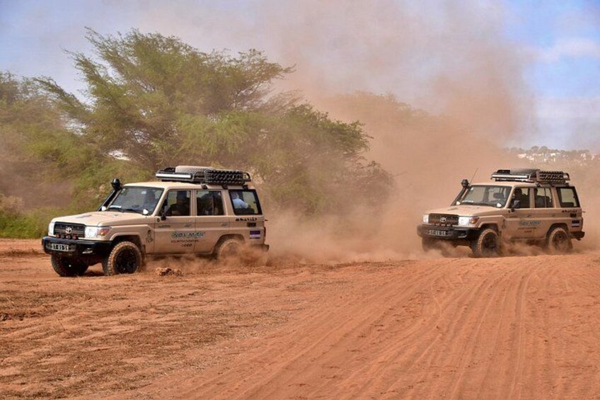 Two off-road vehicles driving on a dusty path with trees in the background. 2