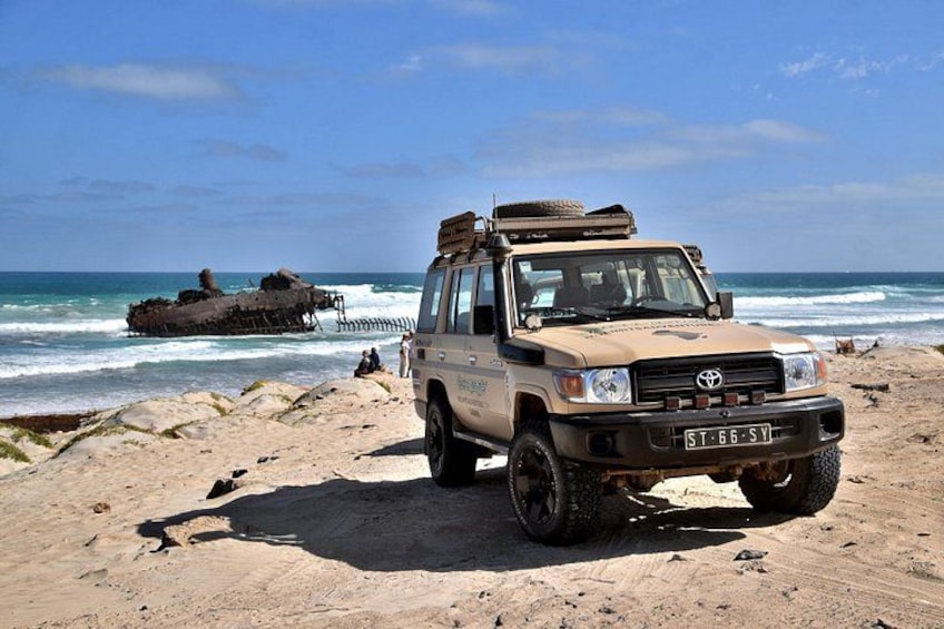 Ein beiger SUV steht auf einem sandigen Strand, im Hintergrund schlagen Wellen. 4
