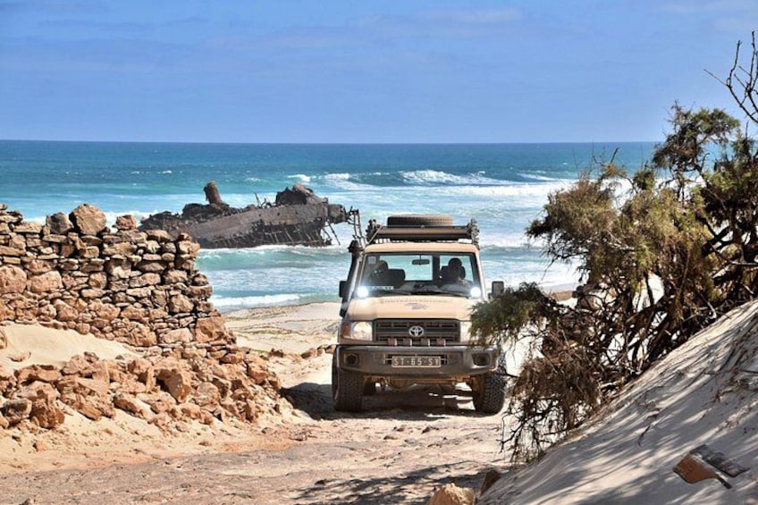 Ein Fahrzeug am sandigen Strand, im Hintergrund schwellende Meereswellen. 5