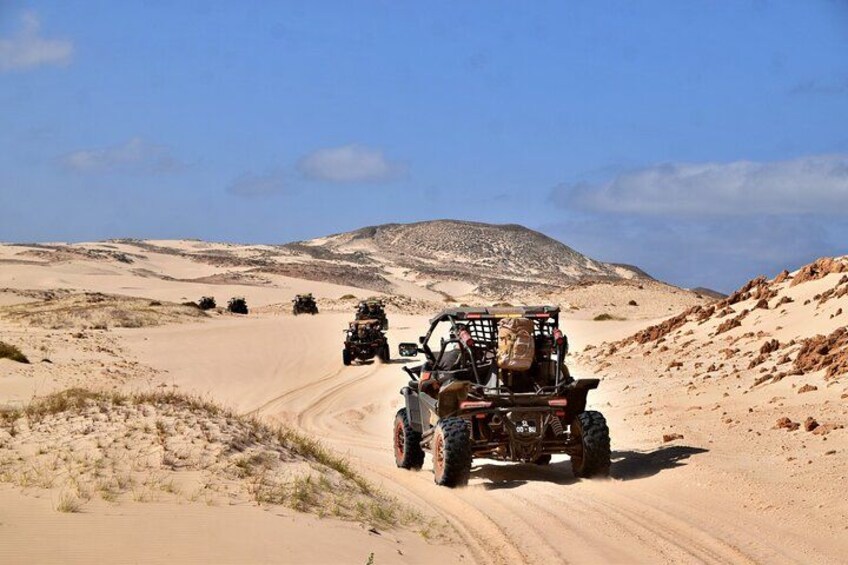 Off-road vehicles on a sandy path in a desert landscape with dunes and a clear sky. 4