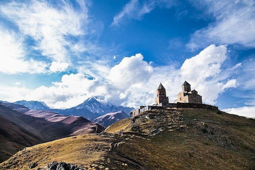 A historic building on a hill with mountains in the background. 1