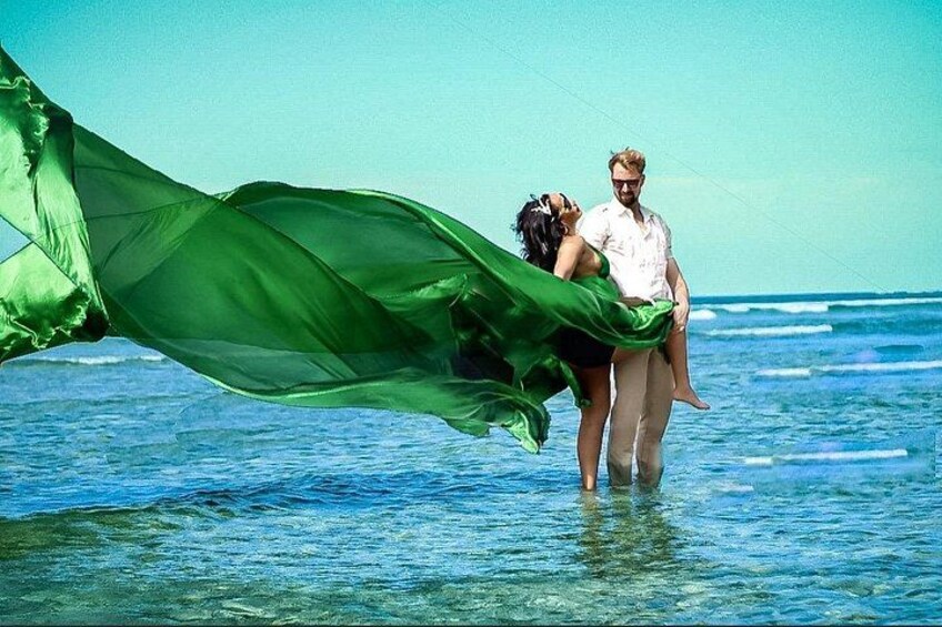 A couple in shallow water with a green fabric flowing in the wind. 1