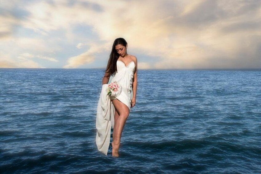 A person in a white dress standing in the ocean with a bouquet of flowers. 5