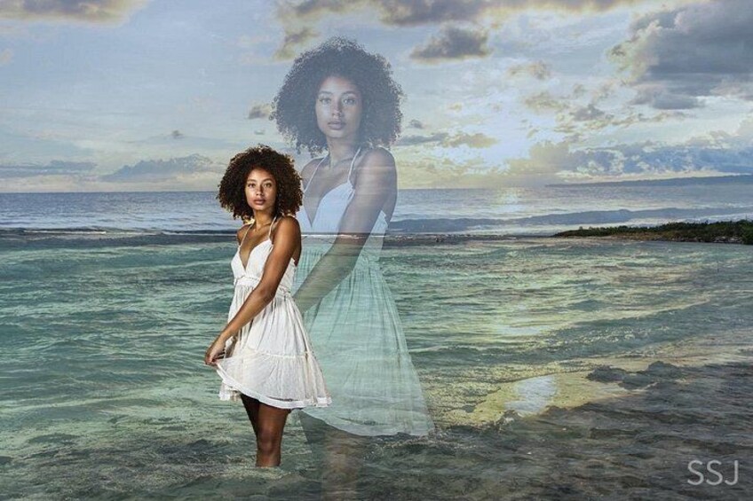 A person standing in shallow water with a beach and ocean in the background. 3