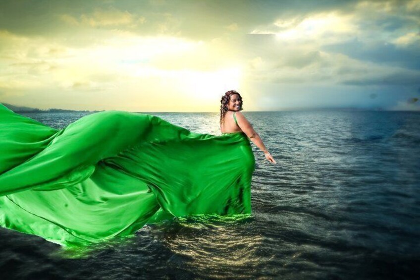 A person in a flowing green dress standing in water with a sunset in the background. 5