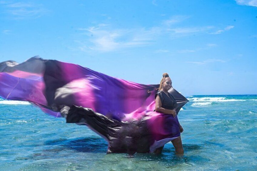 A person standing in shallow water with a flowing purple and black fabric. 2