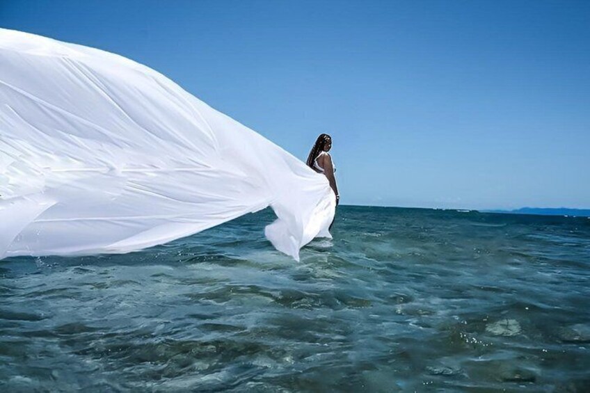 A person in a white dress standing in the ocean with a white cloth flowing in the water. 4