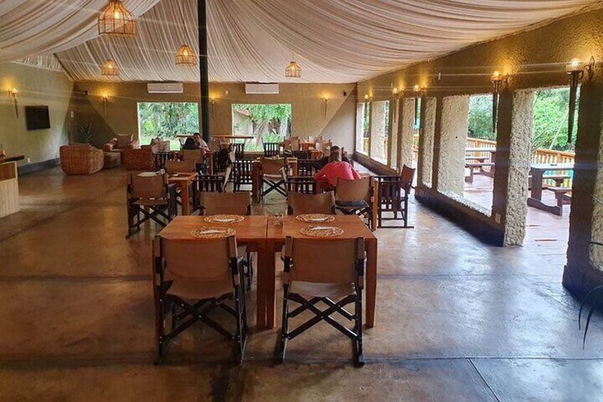 An indoor dining area with tables and chairs, large windows, and a covered ceiling. 2