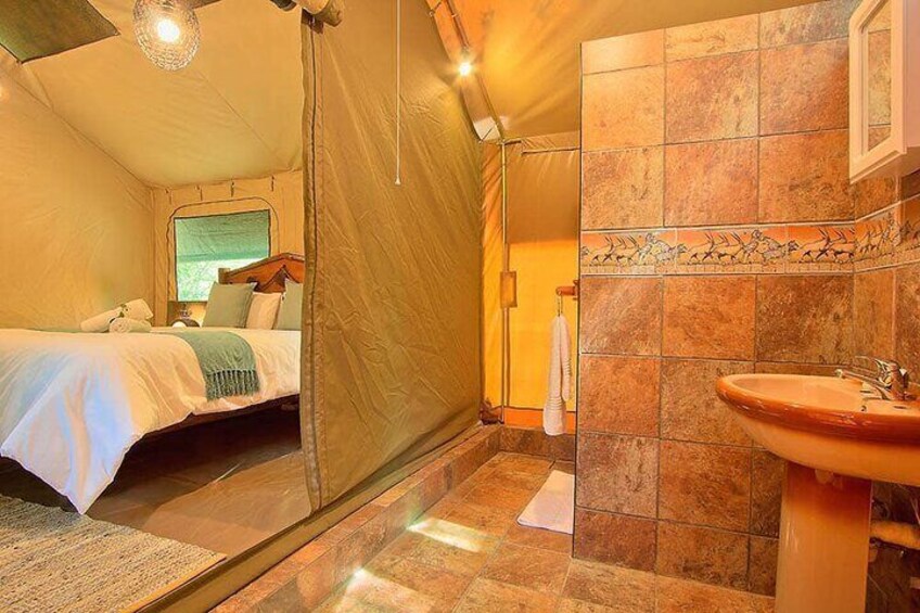 A cozy tented room with a bed, a sink, and a shower area. 3