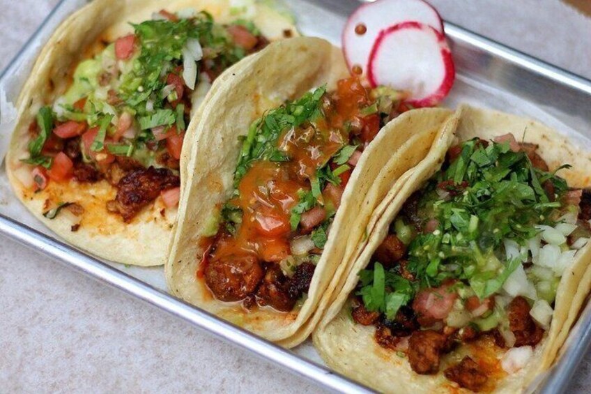 Three tacos with toppings, a radish, and a metal tray. 3