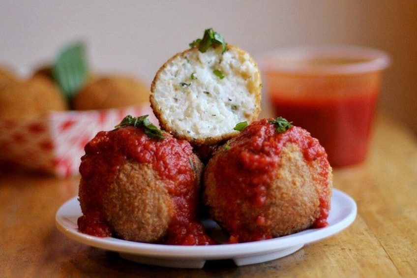 Trois boulettes panées, servies sur une assiette avec une sauce à base de tomates, garnies d’herbes, et une tasse de sauce tomate en arrière-plan. 3