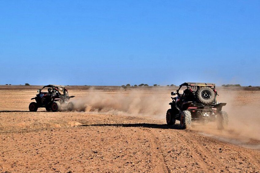 Two off-road vehicles driving on a dusty terrain with a clear sky. 2