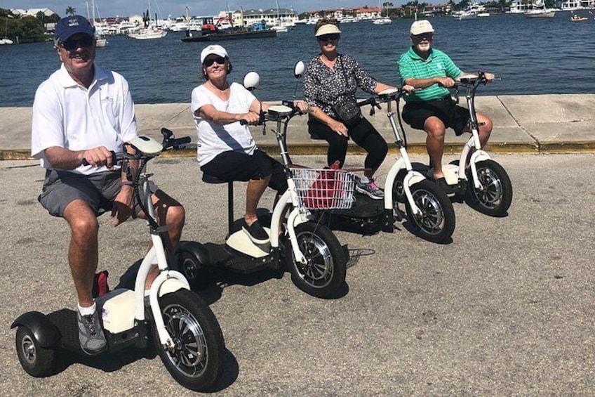 Four people riding electric scooters by a waterfront. 5
