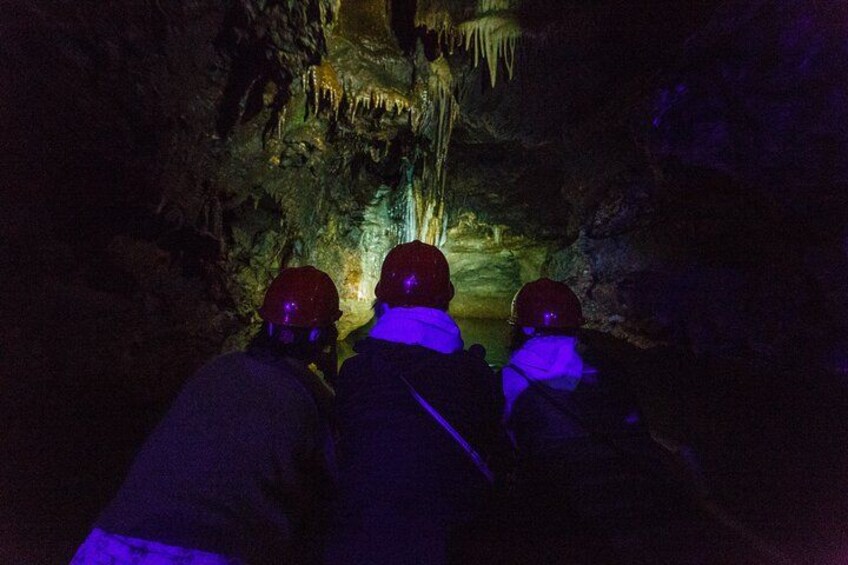 Tre personer med hjälmar och jackor inuti en grotta med stalaktiter. 3
