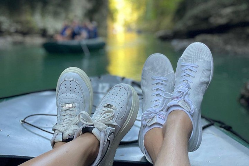A pair of white sneakers on a boat with a river in the background. 1