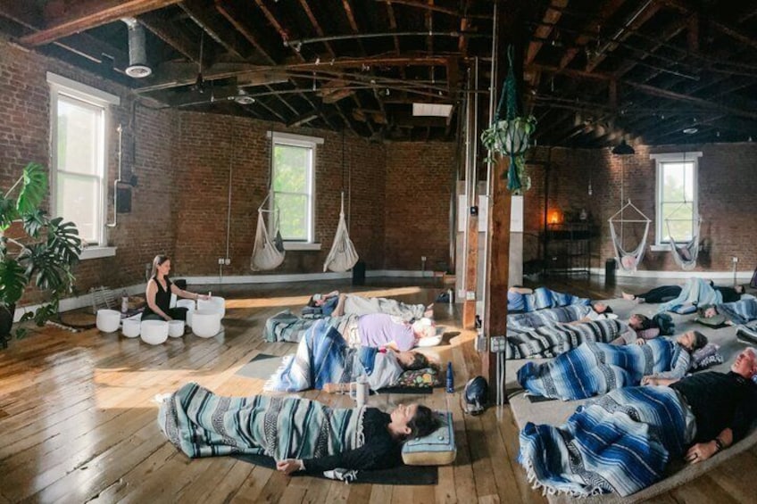 A group of people in a room with wooden floors and brick walls, some lying on mats. 1