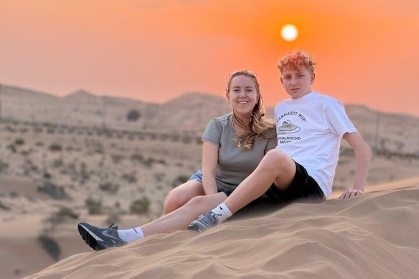 Dos personas sentadas en una duna de arena al atardecer. 2