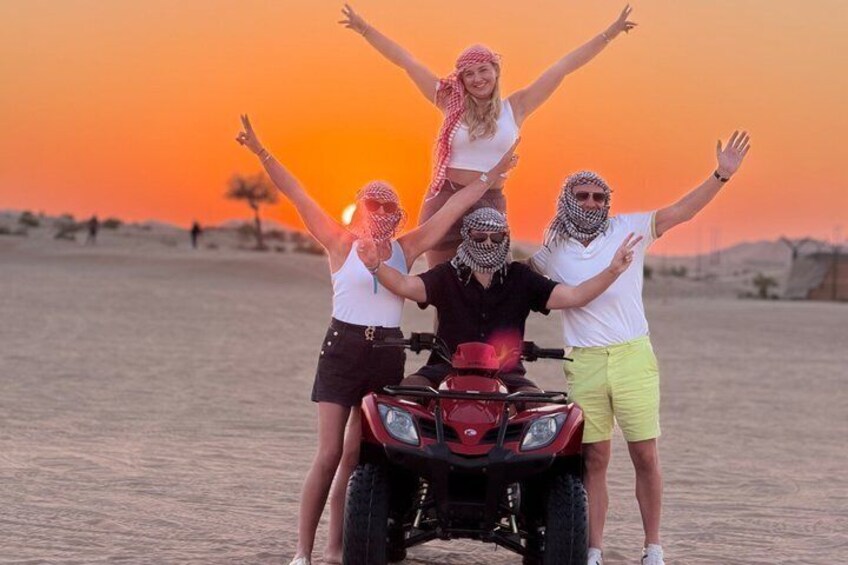 A group of people on a dune with a quad bike, desert landscape, and sunset. 2