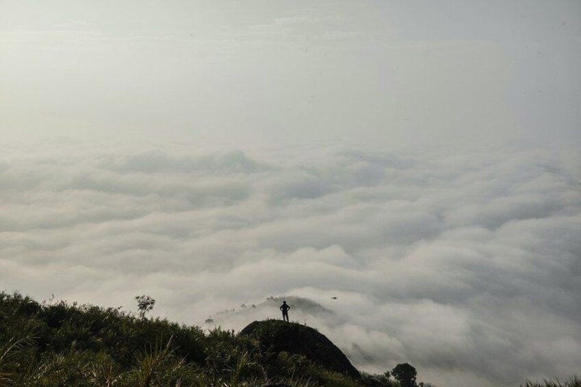 Una persona de pie en una colina con nubes abajo. 1