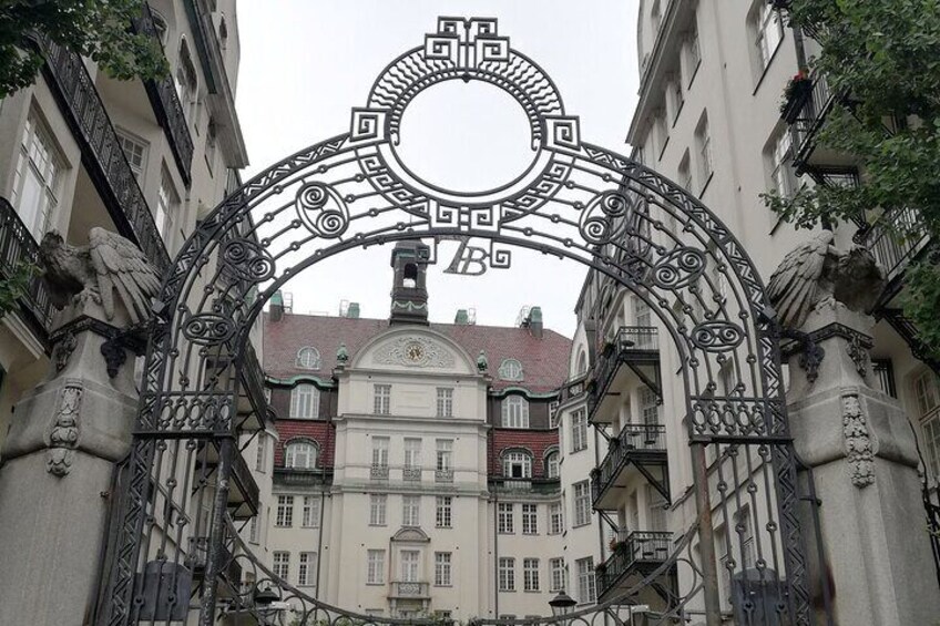 An ornate wrought iron gate with intricate designs, flanked by buildings with classical architecture and balconies. 5