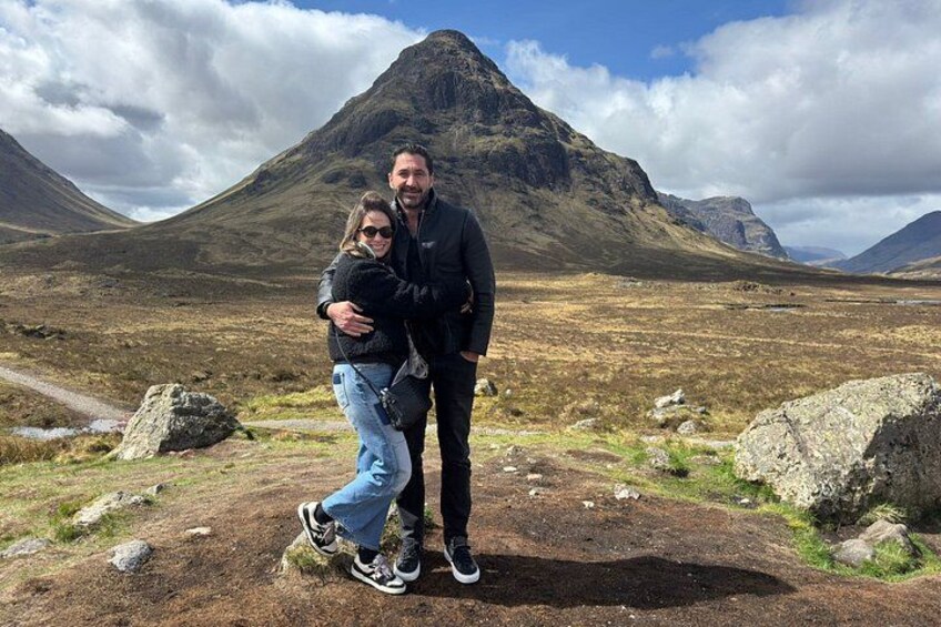 Two people embracing in a mountainous landscape with rocky terrain and a prominent peak in the background. 4