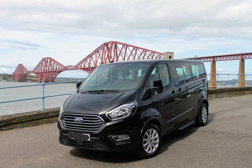 A black Ford van parked on a road with a red bridge in the background. 3